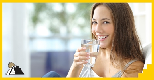 A young adult woman smiling and holding a glass of water