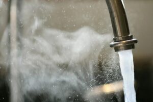Close up of a sink faucet with hot steamy water pouring out